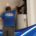 Plumber in a blue Poole’s Plumbing shirt repairs insulated pipes above a residential water heater.